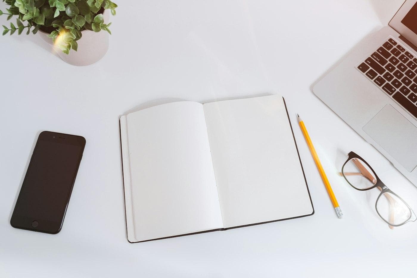 Carnet ouvert, téléphone et crayon sur un bureau blanc
